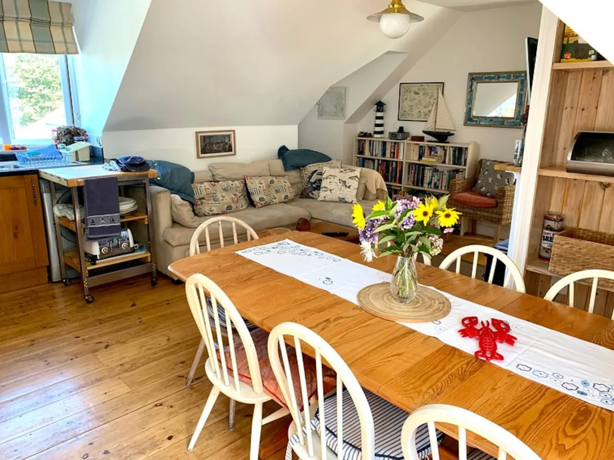 Kittiwake's open-plan upstairs dining and living space, with a wooden table, corner sofa and part of the kitchen