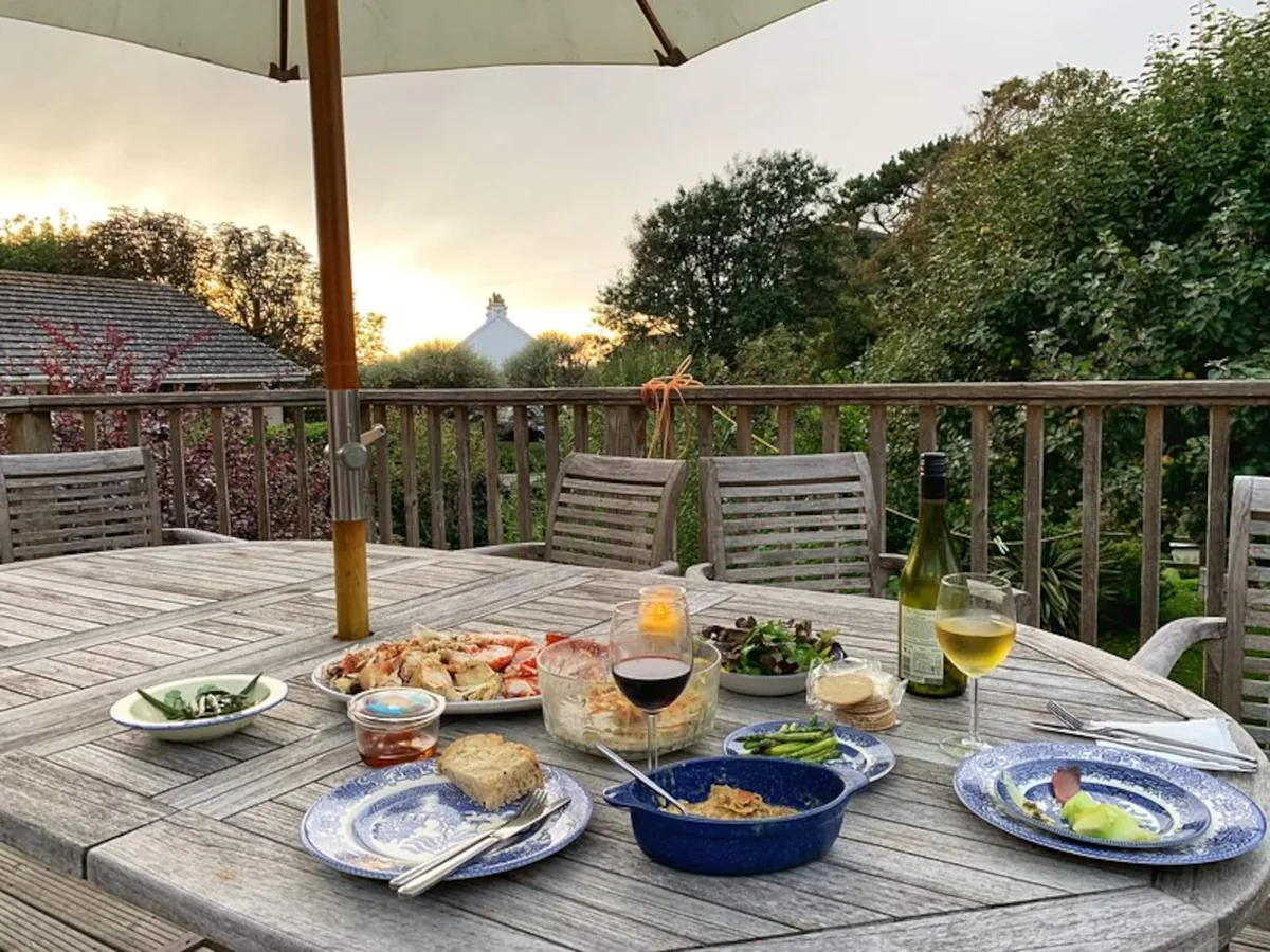 Kittiwake's garden deck in Hope Cove, with an outdoor dining table set for a meal beneath a parasol