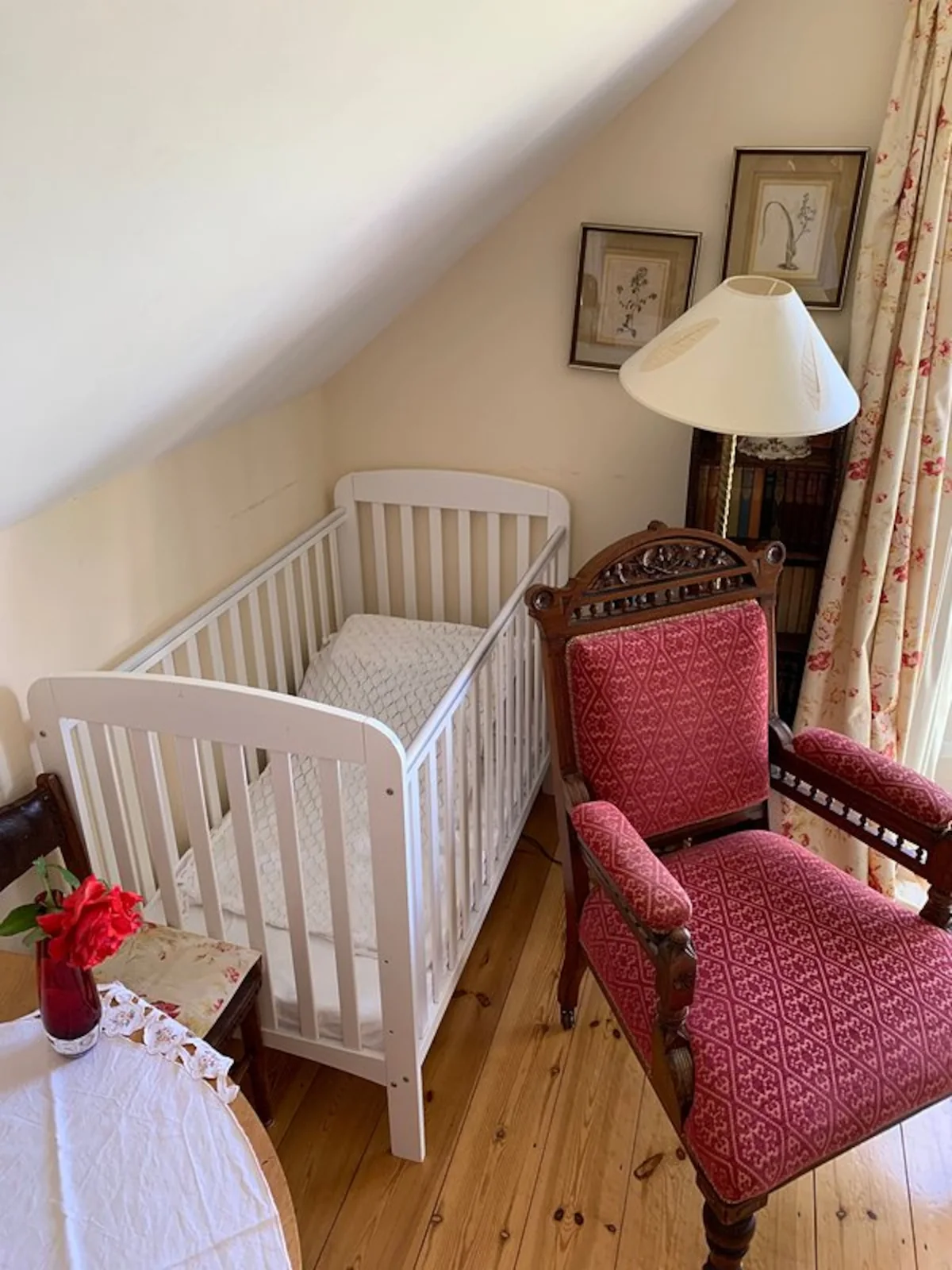 A cot and an upholstered armchair beneath the sloping ceiling at Kittiwake