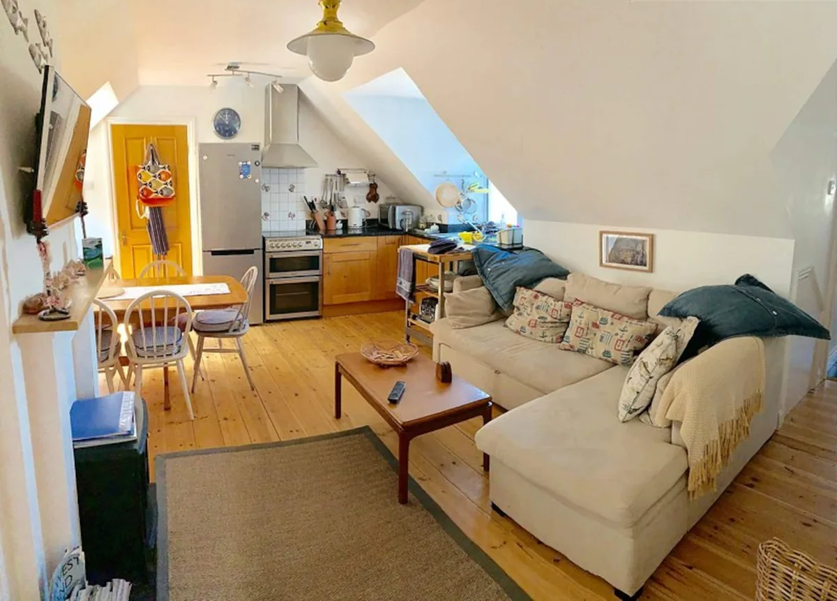 Kittiwake's open-plan upstairs living room and kitchen, with a corner sofa, dining table and fitted kitchen beneath the sloping ceiling
