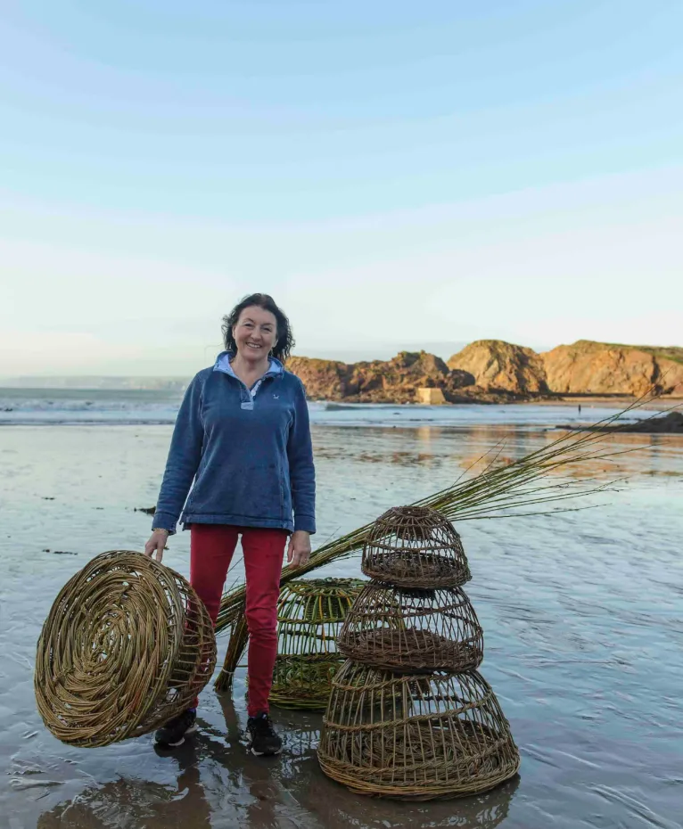 Willow crab pots, a woven basket and a bundle of withies on the beach at Hope Cove, with their maker