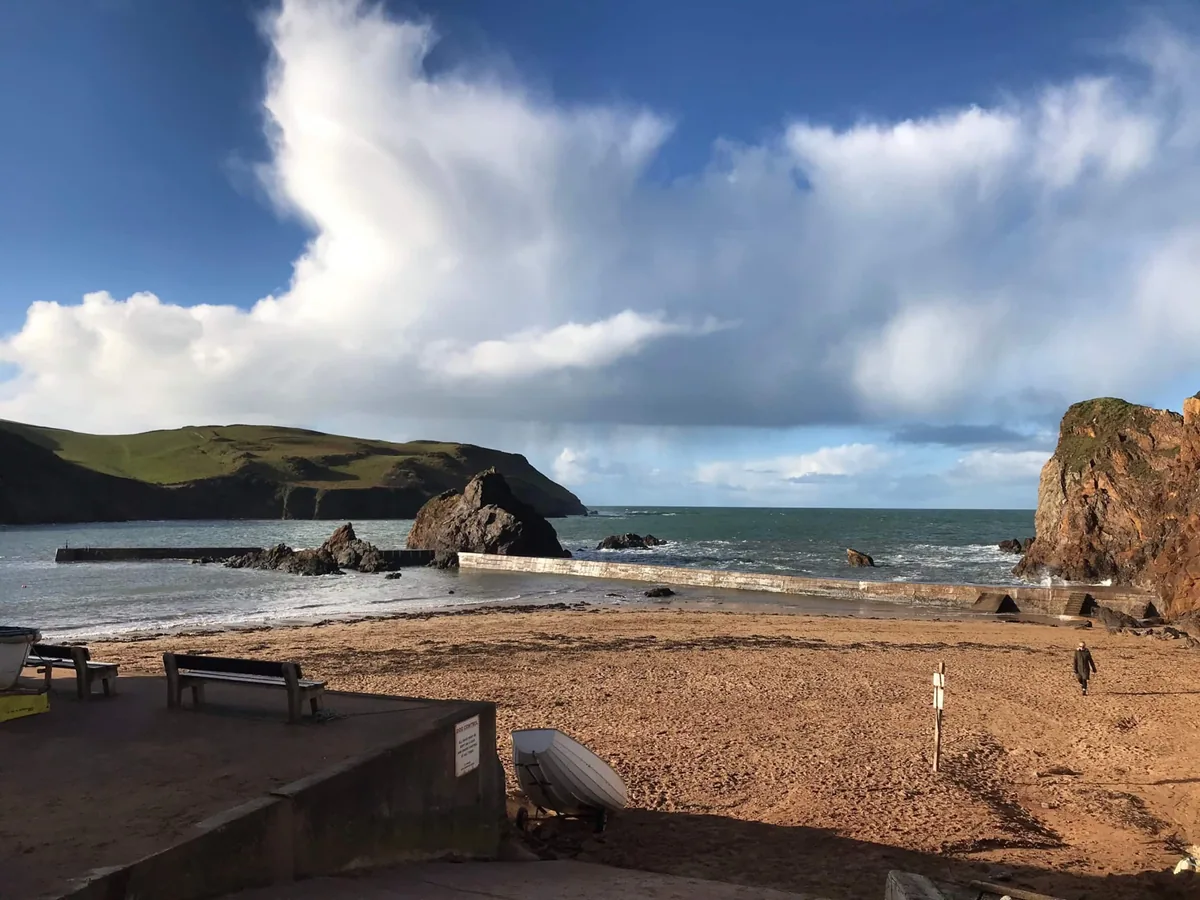 Hope Cove beach, with sand, rocky outcrops, sea walls and green headland beneath a blue sky