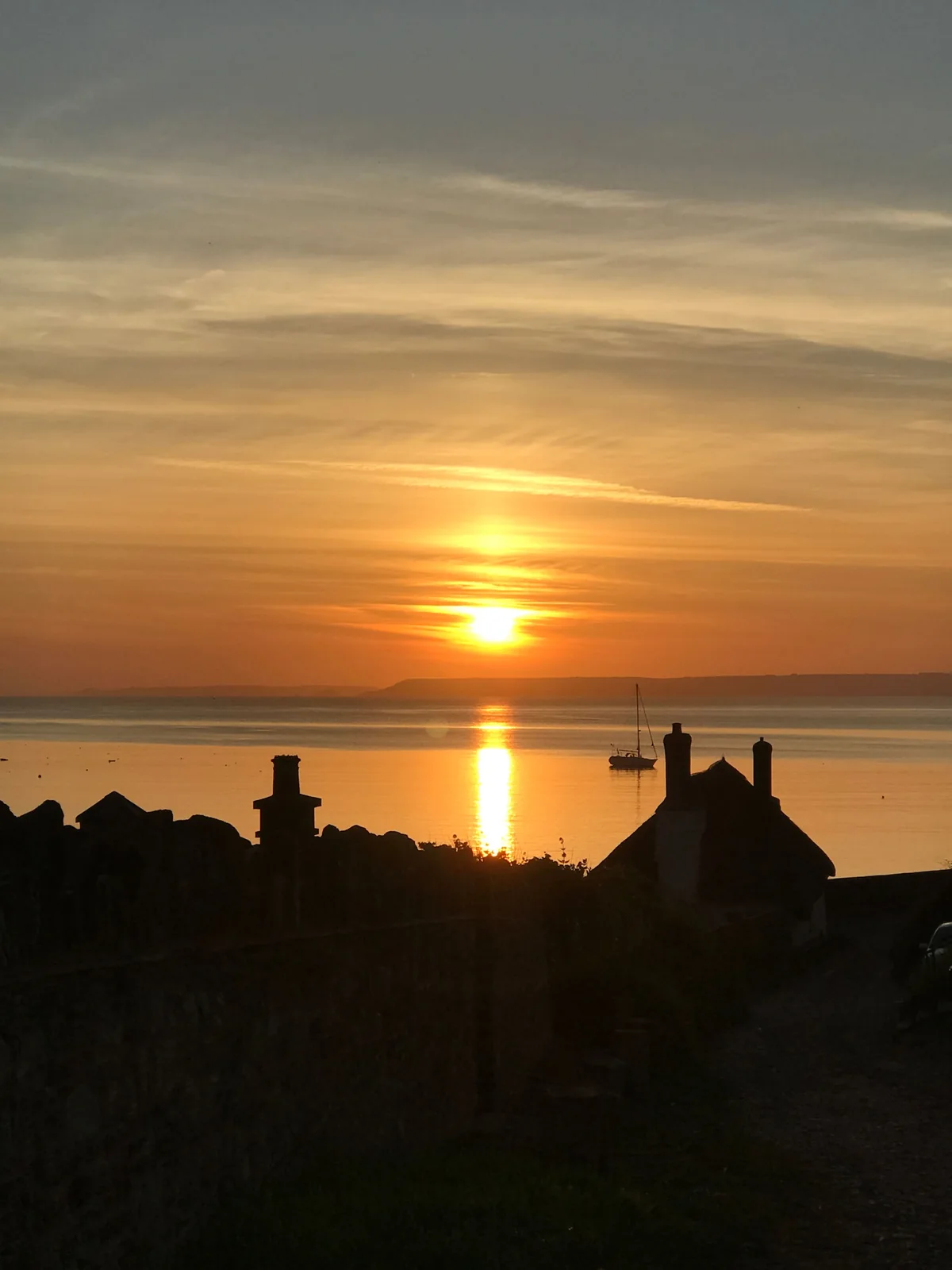 Sunset over the sea at Hope Cove, with a sailing boat and cottages silhouetted in the foreground
